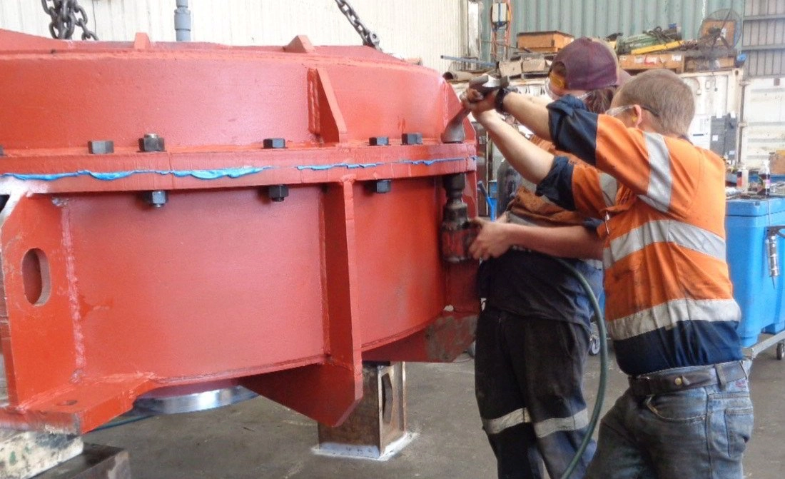Two fitters in hi-vis assembling a large red-painted machinery housing in the workshop