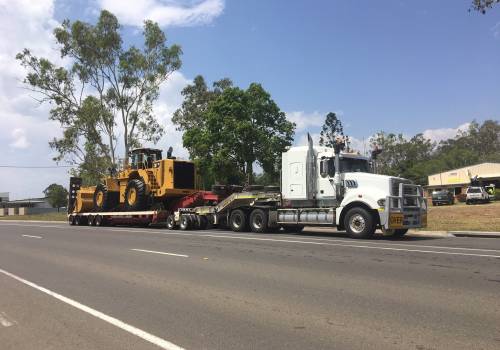ABC prime mover hauling a Caterpillar wheel loader on a low loader float through a Central Queensland town