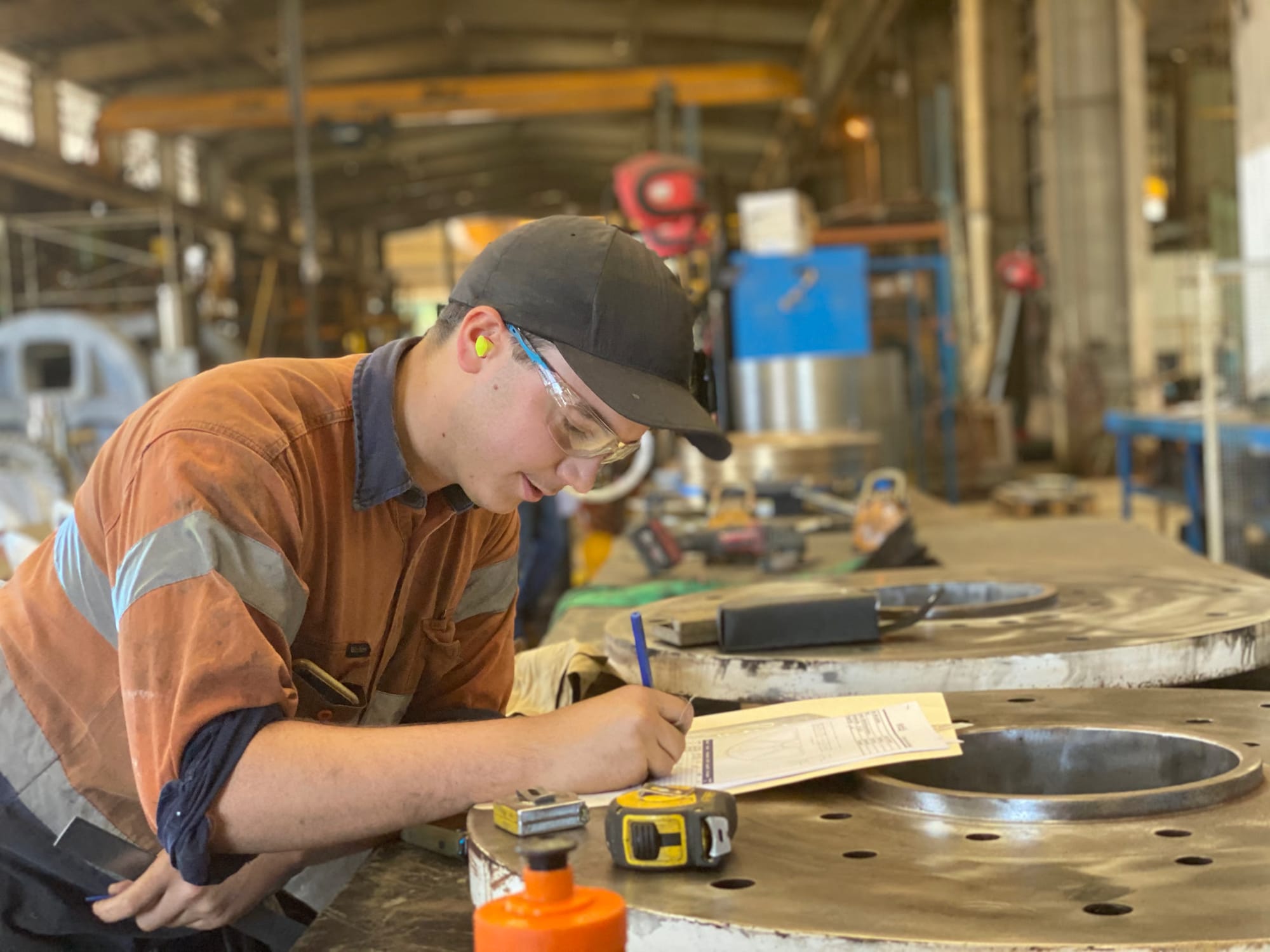 ABC tradesperson recording QA measurements on a large machined flange plate in the workshop